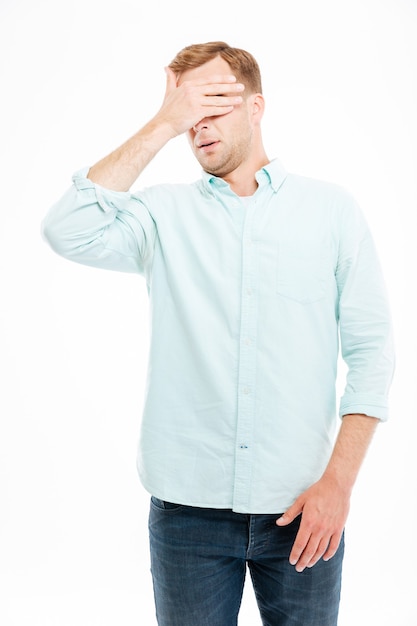 Handsome young businessman covered his eyes by hand over white wall