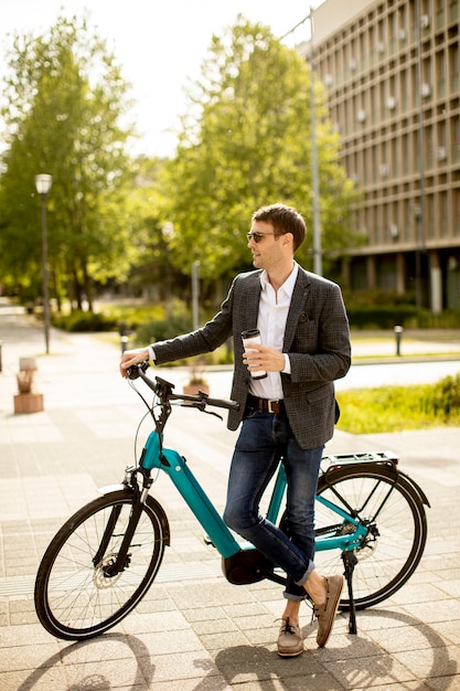 持ち帰り用のコーヒーカップと電動自転車でハンサムな青年実業家