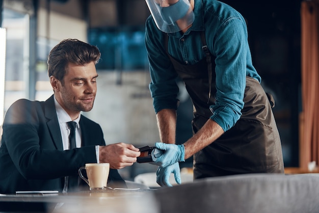 Handsome young businessman making a contactless payment while sitting in the restaurant