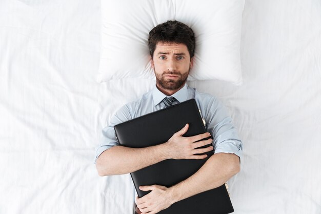 handsome young businessman in the morning in bed lies holding case bag