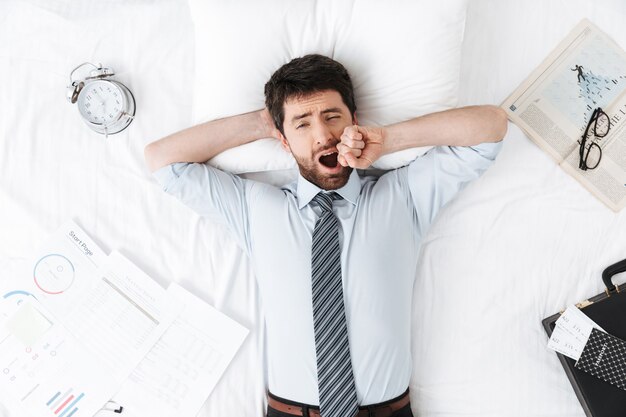 handsome young businessman in the morning in bed lies yawning