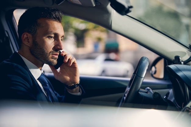 Handsome young businessman in official clothes with watch on hand talking on mobile phone and driving car