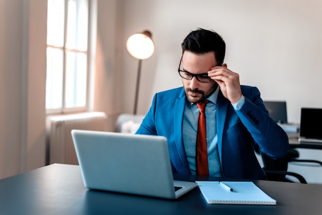 Handsome young businessman reading something on laptop.