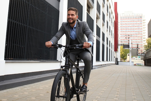 Handsome young businessman riding bicycle outdoors in the city.