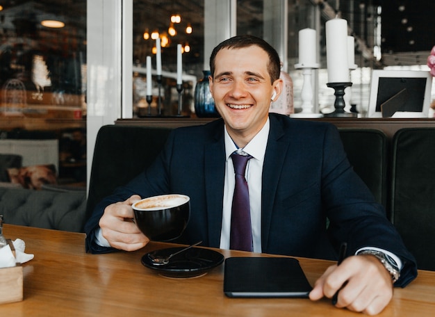 Красивый молодой бизнесмен улыбается и пьет кофе в кафе. мужчина в костюме с кофе.