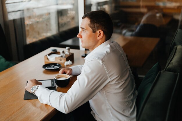 Handsome young businessman smiles and drinks coffee in a cafe. man in a suit with coffee.