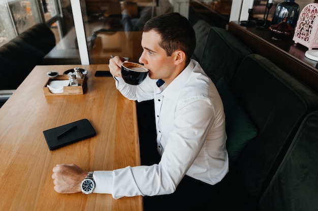 Handsome young businessman smiles and drinks coffee in a cafe. man in a suit with coffee.