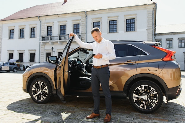 Handsome young businessman talking on the phone while standing near his car outdoors