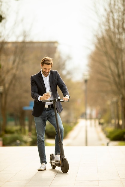 Handsome young businessman using mobile phone  on electric scooter