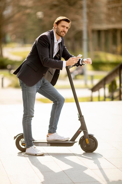 Handsome young businessman using mobile phone  on electric scooter