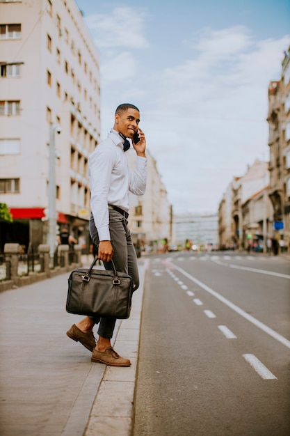 Handsome young businessman using a mobile phone while ceossing a street