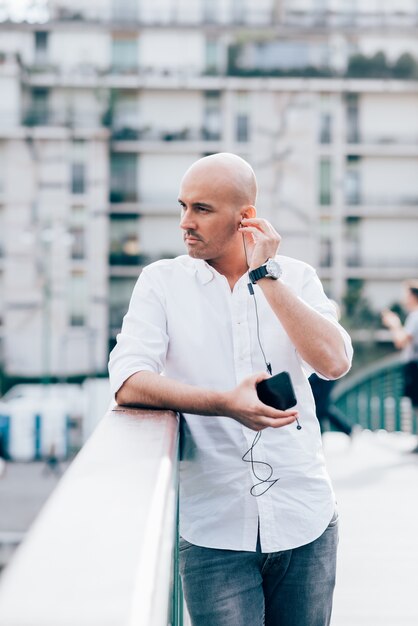 Handsome giovane uomo d'affari in una camicia bianca appoggiato sul corrimano e ascoltare musica