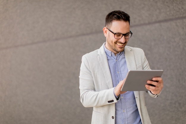 Handsome young businessman with digital tablet by the grey wall