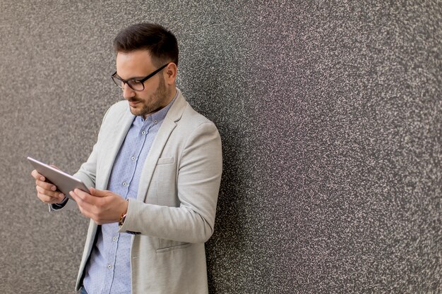 Handsome young businessman with digital tablet by the grey wall