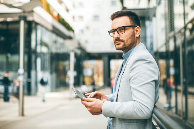 Handsome young businessman with digital tablet by the office building