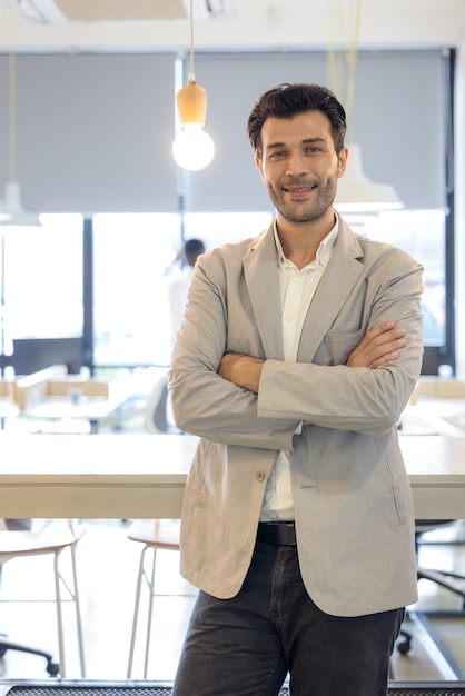 Foto bel giovane uomo d'affari con le braccia conserte in ufficio. uomo allegro sicuro di sé con il ritratto di mani incrociate. affari, successo, persone, concetto di stile di vita in ufficio