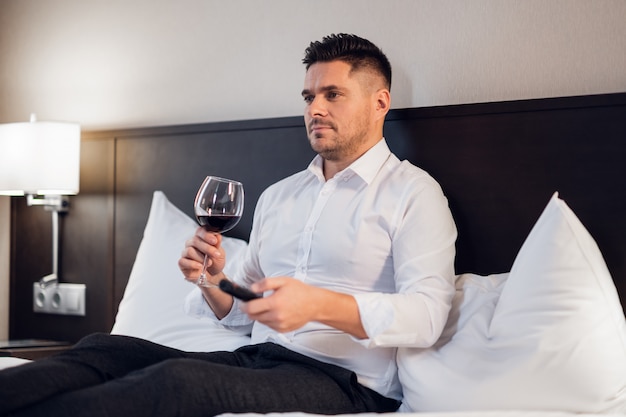 A handsome young businessman with a glass of red wine in bed