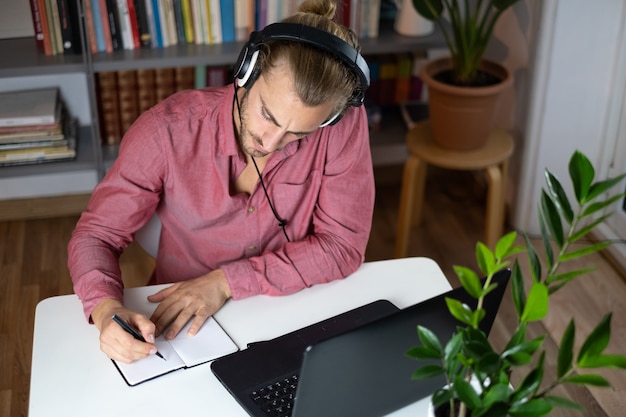 Handsome young caucasian man using computer working and writing at home and talking with headphones