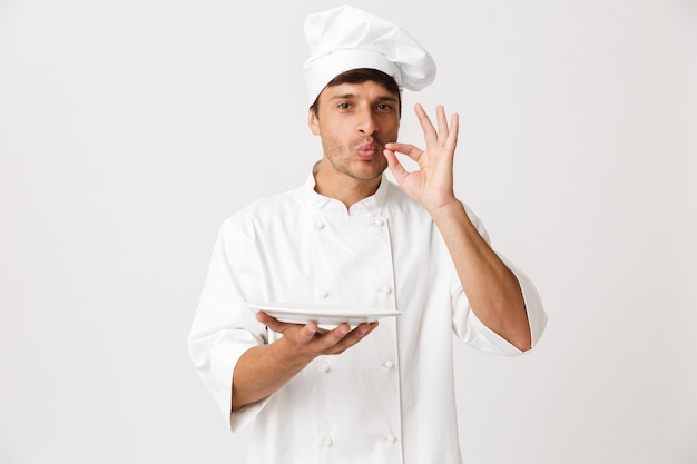 Handsome young chef isolated on white holding plate.