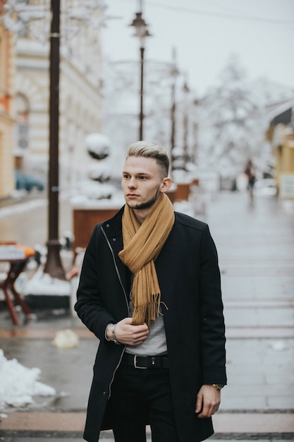 Handsome young confident man in a black winter outfit with a brown scarf strolling around the city