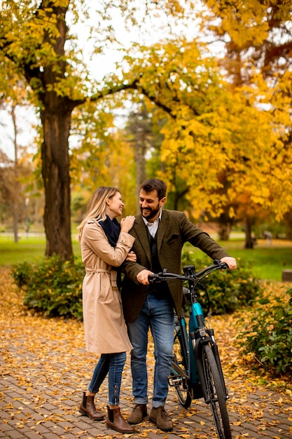 Handsome young couple in the autumn park with electrical bicycle