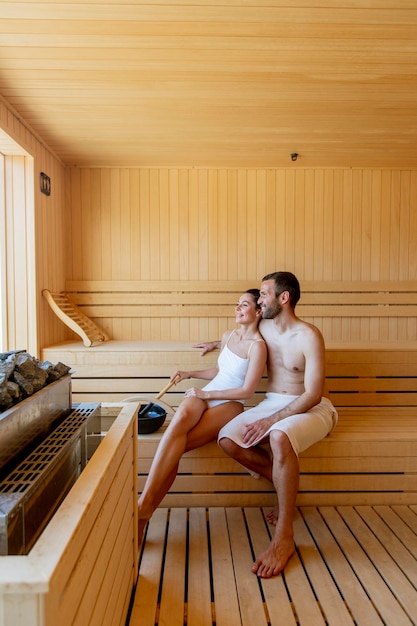 Giovani coppie belle che si rilassano nella sauna e guardano la foresta d'inverno attraverso la finestra