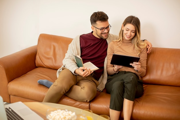 Handsome young couple using digital tablet together while sitting on sofa at home