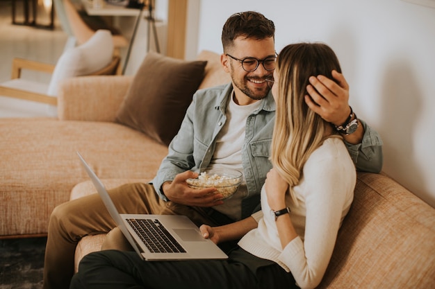 Handsome young couple using laptop together while sitting on sofa at home