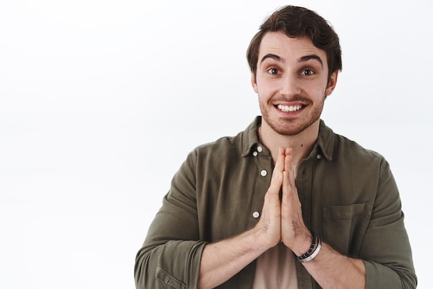 Handsome young cute male student asking classmate cover him hold palms clasped together and smiling do me favour please gesture want help from you standing white background pleading pose