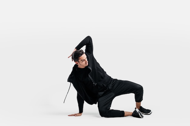 Handsome young dancer wearing a black sweatshirt and black pants is dancing breakdance doing dancing movements on the floor