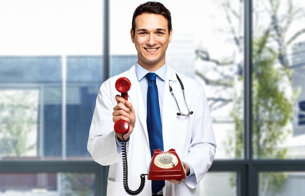 Handsome young doctor portrait holding a red old fashioned phone