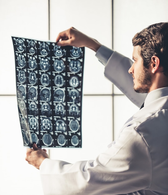 Handsome young doctor in white coat is studying x-ray.