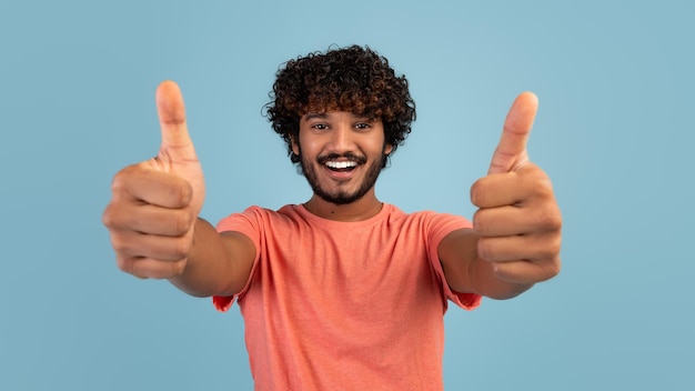 Handsome young eastern guy showing thumb ups on blue panorama