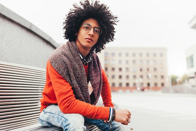 A handsome young Egyptian curly guy sitting on a bench dressed 