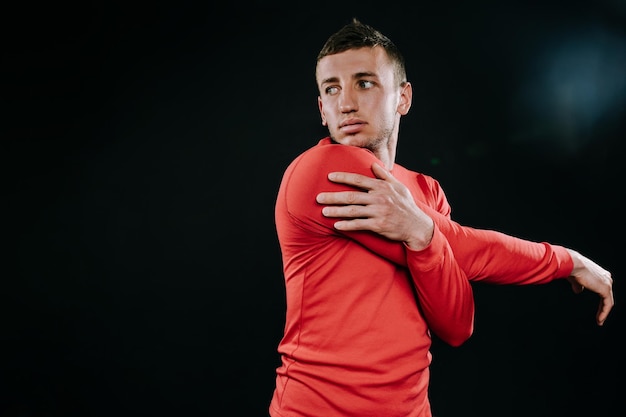 Handsome young European man wearing red sportswear and stretching his arms after a hard workout in dark background Powerful handsome athletic male doing fit Sport motivation Healthy lifestyle
