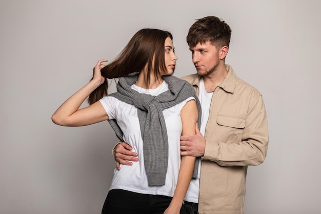 회색 배경에 스튜디오에서 흰색 티셔츠, 빈티지 스웨터, 베이지색 재킷을 입은 세련된 겉옷을 입은 잘생긴 젊은 커플 여성과 잘생긴 남자