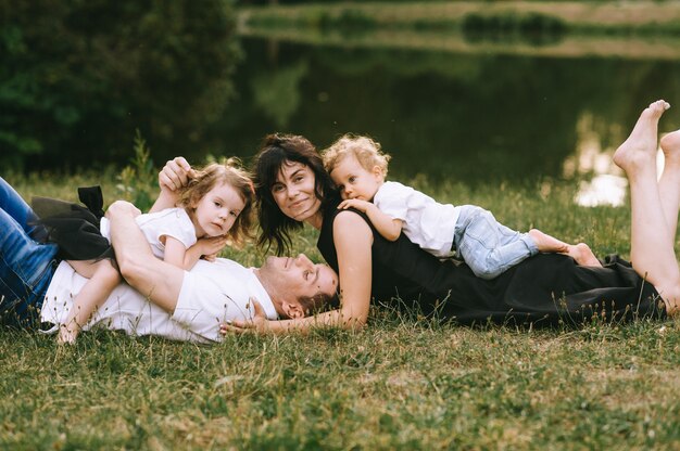 Giovane padre bello e bella madre in natura soleggiata di estate che giocano con i loro piccoli bambini svegli