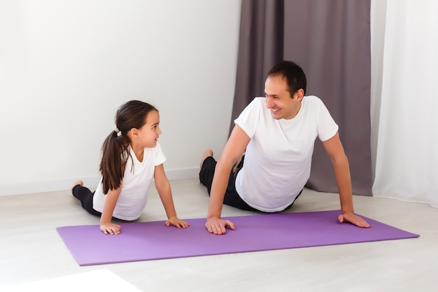 Handsome young father and his cute little daughter are doing reverce plank with leg raise on the floor at home. Family fitness workout.