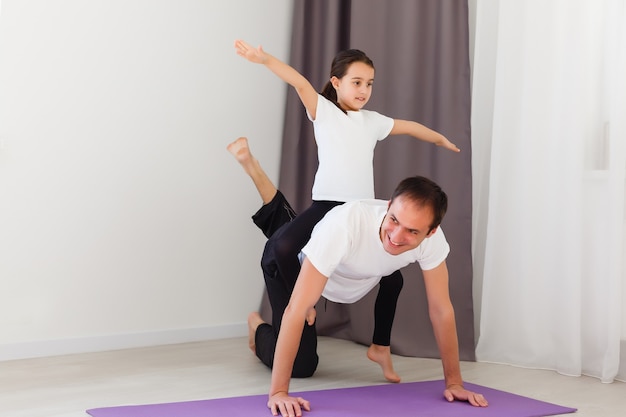 Handsome young father and his cute little daughter are doing reverce plank with leg raise on the floor at home. family fitness workout.