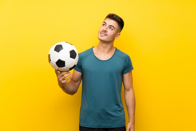 Handsome young football player man over isolated yellow background looking up while smiling