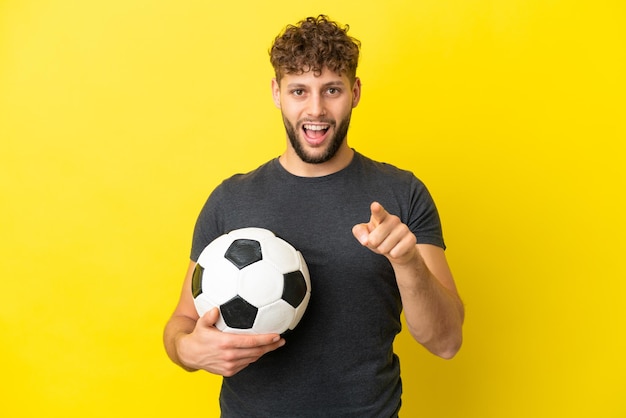 Handsome young football player man isolated on yellow background surprised and pointing front