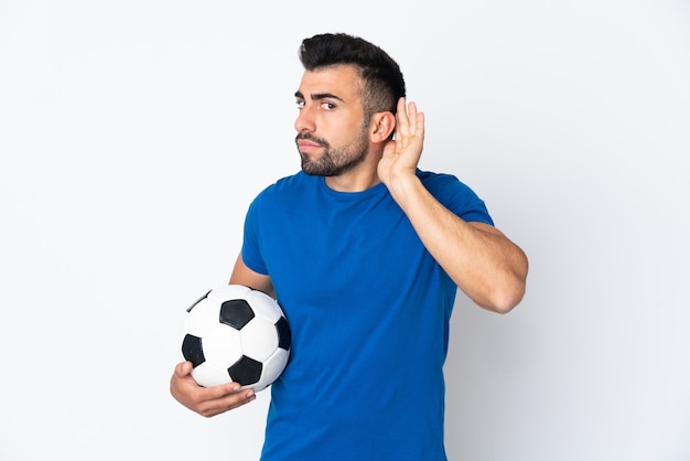 Handsome young football player man over wall listening to something by putting hand on the ear