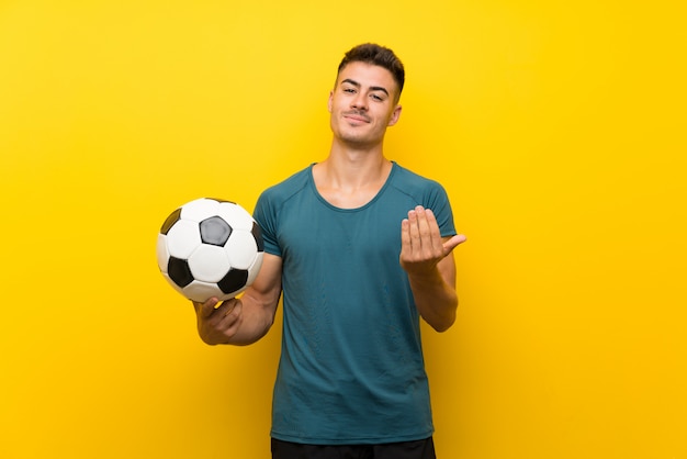 Foto giovane uomo bello del giocatore di football americano sopra la parete gialla che invita a venire con la mano. felice che tu sia venuto