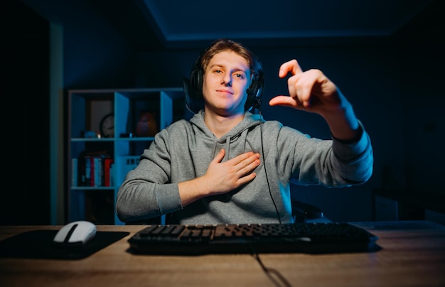 Handsome young gamer in headphones with microphone streaming game at night in a room