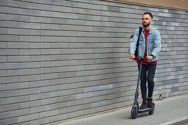 Handsome young guy in casual clothes riding electric schooter outdoors at sunny daytime