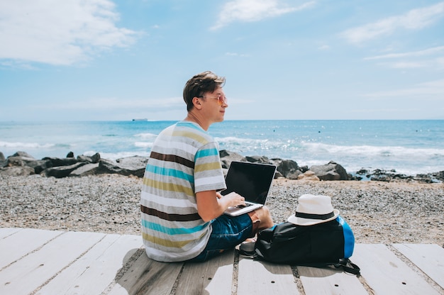 handsome young guy the photographer working with a laptop on the beach