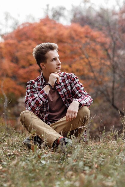 Handsome young guy in plaid shirt sitting in nature on an autumn day