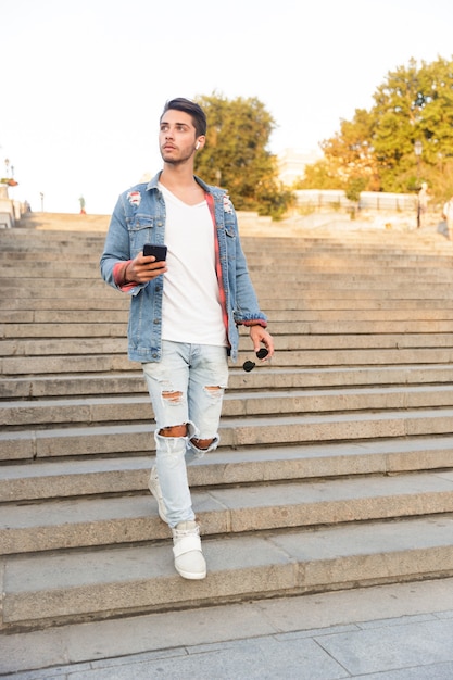 Handsome young guy walking outdoors using mobile phone and listening to music