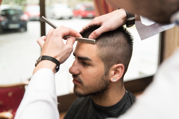 Giovane parrucchiere bello che dà un nuovo taglio di capelli al cliente maschio al salone