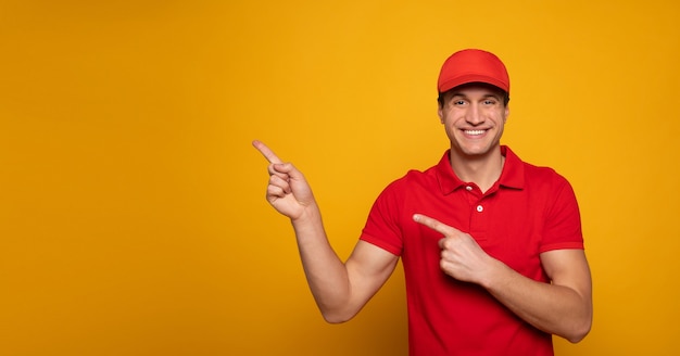 Handsome young happy courier or delivery man in red uniform is posing isolated on yellow background.